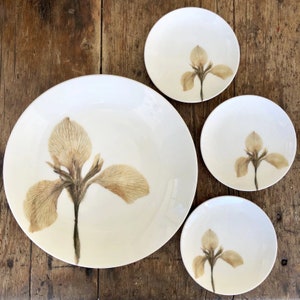 May include: Set of four white ceramic plates with a pressed dried flower design. The plates feature a delicate brown iris flower.