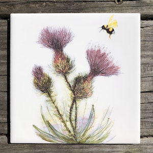 May include: A watercolor painting of a thistle plant with three purple flower buds and a bumblebee flying above. The background is white.