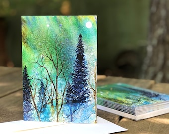 May include: A greeting card with a watercolor painting of a forest scene. The painting features a moon, blue and green trees, and a white background.