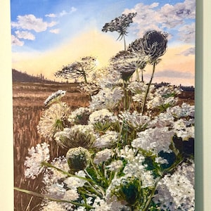 May include: A spiral-bound calendar featuring a painting of Queen Anne's Lace wildflowers in a field. The artwork depicts white flowers with green stems against a backdrop of a sunset sky with clouds. The painting has a textured, impressionistic style.