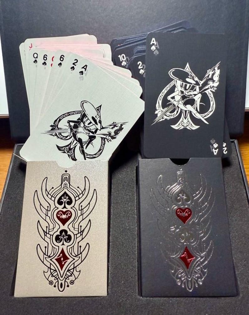 Pu&ograve; includere: Un mazzo di carte da gioco dal design unico. Le carte presentano un'illustrazione in bianco e nero su sfondo nero. Le facce delle carte sono bianche con semi e numeri neri. Gli astucci sono argentati e neri con un design rosso e nero.