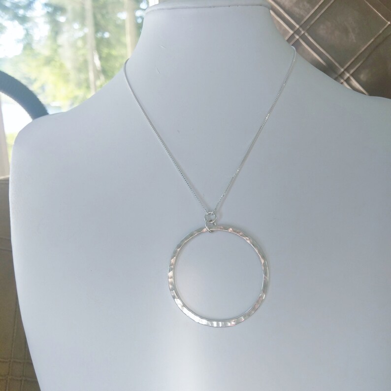 Puede incluir: Un collar de plata con un colgante circular martillado.