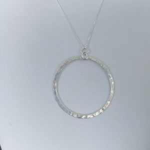 Puede incluir: Un collar de plata con un colgante circular martillado.