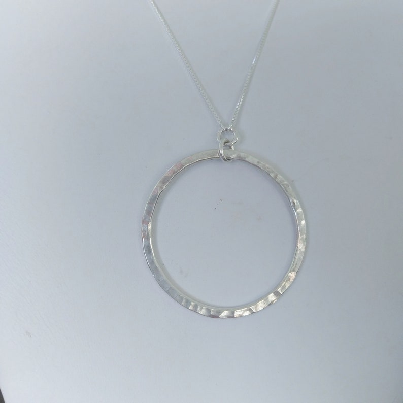 Puede incluir: Un collar de plata con un colgante circular martillado.