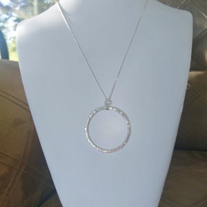 Puede incluir: Un collar de plata con un colgante circular martillado.