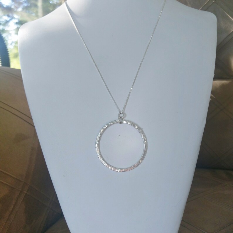 Puede incluir: Un collar de plata con un colgante circular martillado.