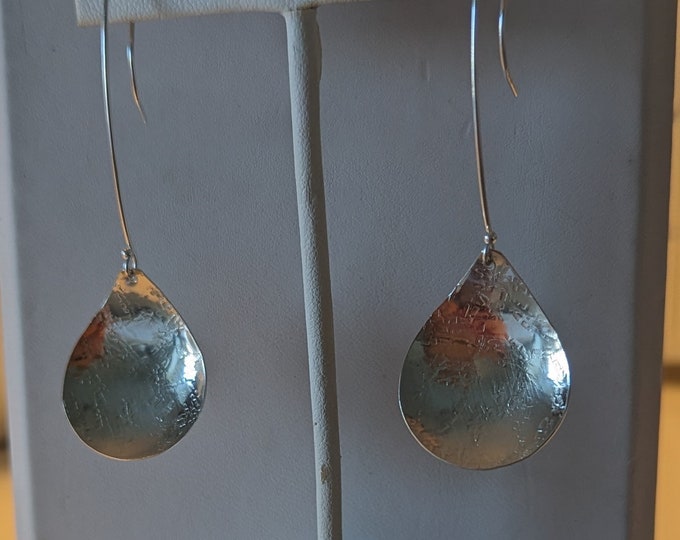 Sterling raw silk textured teardrop earrings dangle from long wires.  Slight concave form.