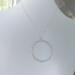Puede incluir: Un collar de plata con un colgante circular martillado.
