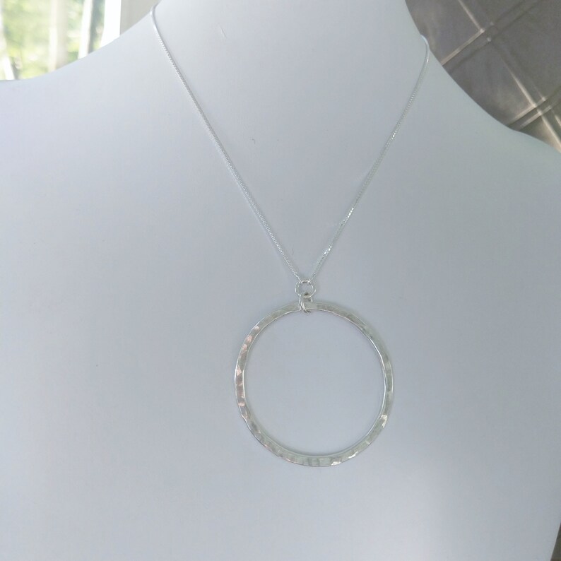 Puede incluir: Un collar de plata con un colgante circular martillado.