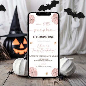K&ouml;nnte beinhalten: Ein Smartphone zeigt eine Einladung zum Thema Halloween mit dem Text "our little pumpkin is turning one!" in rosa Schrift. Die Einladung enth&auml;lt den Namen "Olivia" und Veranstaltungsdetails. Der Hintergrund zeigt K&uuml;rbisse, Flederm&auml;use und einen Hexenhut.
