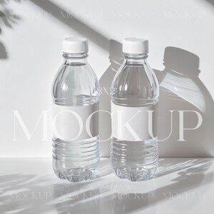 May include: Two clear plastic water bottles with white labels and white caps on a white surface with shadows from a plant.