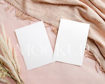May include: Two blank white cards on a pink background with a light brown scarf and white pampas grass.