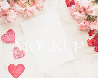 Puede incluir: Una maqueta estilizada con una tarjeta en blanco de 13 x 18 cm con la palabra "MOCKUP" superpuesta. La tarjeta está rodeada de flores rosas y rojas y tres corazones rojos con purpurina, todo dispuesto sobre una superficie de mármol.