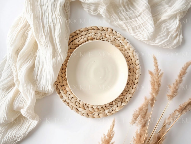 May include: A white ceramic plate on a woven straw placemat with a white cloth and dried pampas grass on a white background.
