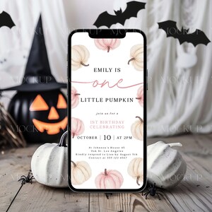 K&ouml;nnte beinhalten: Ein Smartphone zeigt eine Halloween-Einladung mit K&uuml;rbis-Illustrationen und dem Text "Emily is one Little Pumpkin". Das Telefon liegt auf einer Holzoberfl&auml;che mit K&uuml;rbissen, Spinnen und Flederm&auml;usen, was eine festliche Szene ergibt.