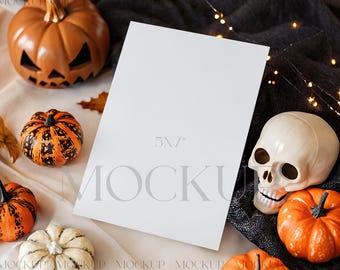 Op de afbeelding: Een Halloween-thema mockup met een blanco kaart van 13x18 cm, omringd door decoratieve pompoenen, een schedel en herfstbladeren. De pompoenen variëren in grootte, kleur en ontwerp, wat een feestelijke en seizoensgebonden presentatie creëert.