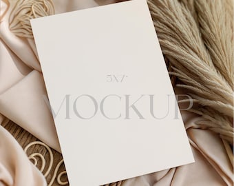 Puede incluir: Una maqueta de tarjeta crema de 5x7 pulgadas con la palabra "MOCKUP" impresa, apoyada sobre una tela beige con hierba de la pampa seca. La tarjeta está centrada, creando una estética minimalista y elegante.