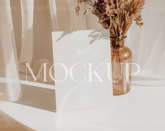 May include: A white 5x7 inch card mockup on a white surface with a vase of dried pampas grass in the background. The card is blank and ready for your design.