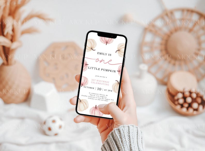 May include: A mobile phone displaying a digital invitation for a first birthday party. The invitation features a watercolor illustration of pumpkins and the text "Emily is one little pumpkin".
