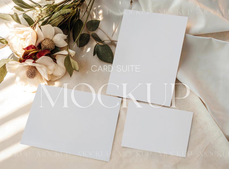 May include: A mockup of a card suite with three blank white cards of different sizes, arranged on a beige fabric surface. A floral arrangement with white and red flowers and green leaves is in the upper left corner. The words "CARD SUITE" and "MOCKUP" are visible.