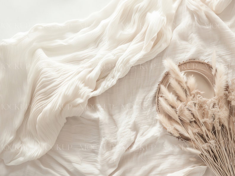 May include: A white plate with a wooden rim sits on a white fabric background. Dried pampas grass is arranged around the plate.
