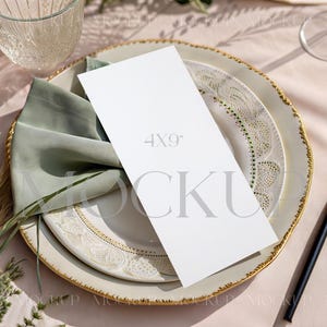 May include: A table setting with a white menu card that reads "4x9" on a decorative plate with a gold rim. A green napkin is tucked under the card. Gold cutlery and a glass are also visible.