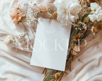 May include: A white card with the text "5x7" printed on it, surrounded by a bouquet of white and beige flowers on a cream-colored fabric background.