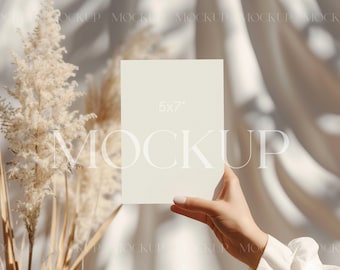 Può includere: Un biglietto color crema di 5x7 pollici tenuto davanti a uno sfondo morbido e neutro. La parola "MOCKUP" è sovrapposta all'immagine. Erba della pampa secca e tessuto drappeggiato aggiungono consistenza e profondità.