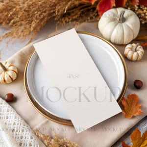 May include: A white plate with a gold rim holds a blank 4x8 inch card, surrounded by fall-themed decorations. Miniature pumpkins, fall leaves, and wheat stalks create a seasonal aesthetic. The scene is set on a beige cloth.