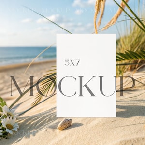 Puede incluir: Una tarjeta rectangular vertical blanca con el texto 5X7 MOCKUP en fuente gris oscuro. La tarjeta está colocada en una playa de arena con margaritas blancas, hierba de playa verde y una concha marina visibles en el primer plano.