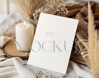 May include: A 5x7 inch blank card mockup with the word "MOCKUP" in gray. A lit white candle sits on a wooden slice, with dried plants and a patterned blanket in the background. The scene has a neutral, warm aesthetic.