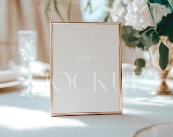 May include: A gold-toned frame with a white mat and a blank white interior. The frame is sitting on a white tablecloth with a glass of water and a plate in the background. The frame is 8x10 inches.