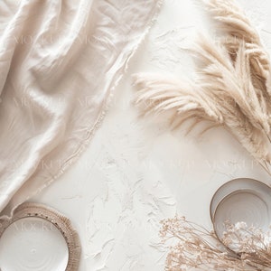 May include: A flat lay featuring a white textured background with a beige linen fabric, two white ceramic plates, dried pampas grass, and dried baby's breath.