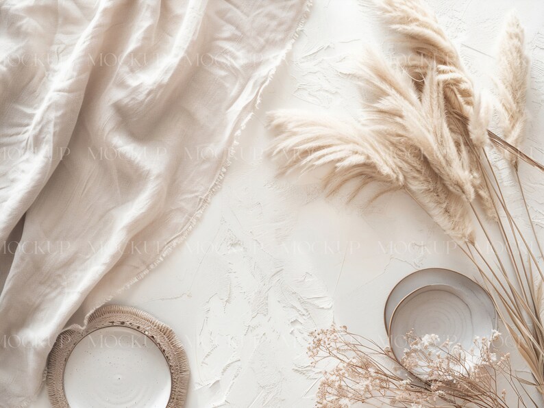 May include: A flat lay featuring a white textured background with a beige linen fabric, two white ceramic plates, dried pampas grass, and dried baby's breath.