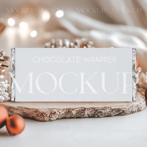 May include: A white chocolate wrapper mockup with the text "CHOCOLATE WRAPPER MOCKUP" on a wooden slice, surrounded by Christmas ornaments and pine cones. The scene is festive with warm lighting and a soft background.