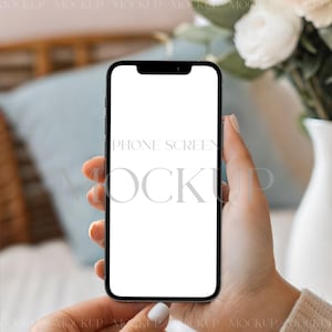 May include: A black smartphone with a blank white screen is held in front of a soft background. The phone's screen displays the text "PHONE SCREEN MOCKUP". The background includes a vase of flowers and a light blue pillow.