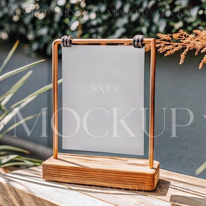 Puede incluir: Un marco de cobre con un cartel blanco en blanco, de 20,3 x 25,4 cm, sobre un soporte de madera. El cartel está colocado sobre una mesa de madera con una planta verde y una rama marrón en el fondo.