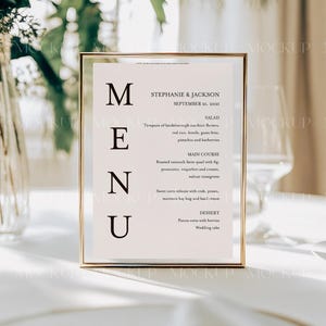May include: A gold-framed menu sign with a white background and black text. The menu lists the names Stephanie & Jackson, the date September 21, 2021, and the menu items: Salad, Main Course, and Dessert.