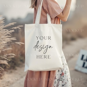 Könnte beinhalten: Eine weiße Canvas-Tragetasche mit schwarzem Text, der "Your design here" lautet. Die Tasche wird von einer Person getragen, die ein rosa Hemd und einen Blumenrock trägt.