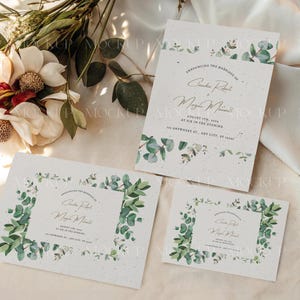 May include: A mockup of wedding stationery, including invitations and RSVP cards, featuring a botanical design with eucalyptus leaves. The text announces the marriage of two people. The stationery is arranged on a neutral surface with floral accents.