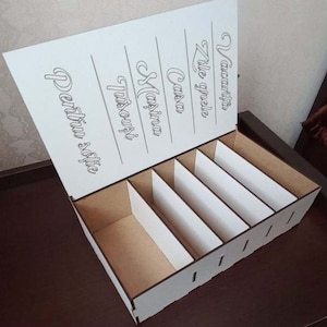 Può includere: Scatola di legno bianca con sei scomparti e un coperchio. Il coperchio ha le parole "Vacanta", "Zile grele", "Casa", "Masina", "Trusou", e "Pentru sotie" scritte su di esso.