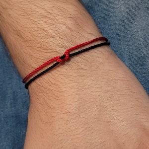 May include: A red and black string bracelet on a person's wrist.