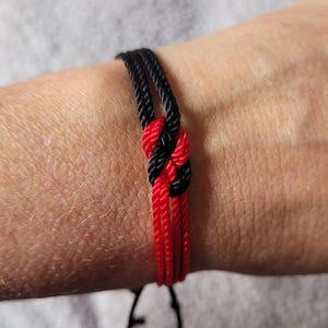 May include: A red and black braided friendship bracelet with a knot in the center.