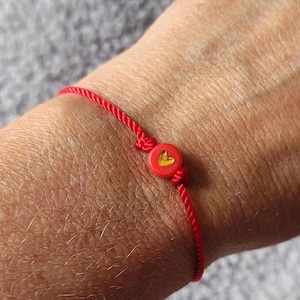 May include: A red string bracelet with a small red heart charm with a gold heart inside.