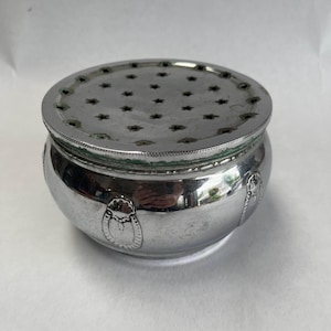 Pode incluir: Um recipiente redondo prateado com uma tampa perfurada. A tampa apresenta recortes em forma de estrela. O recipiente tem um corpo bulboso com desenhos ovais decorativos. O metal tem um aspeto ligeiramente manchado.