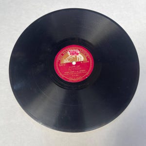Pode incluir: Um disco de vinil preto vintage com um rótulo vermelho e dourado. O rótulo diz "HIS MASTER'S VOICE" e apresenta o título "SOUND OFF" de Vaughn Monroe & His Orchestra. O disco é de 78 RPM.