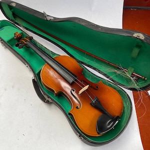 Può includere: Un violino marrone con manico e corde nere in una custodia nera e verde. Il violino è in una custodia con una fodera verde.