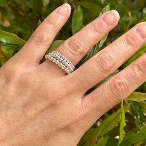 May include: A set of three silver beaded rings stacked on a finger. The rings are made of small, round beads that are evenly spaced.