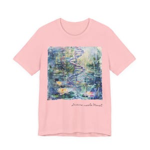 May include: A light pink short-sleeve t-shirt featuring a square graphic print of a DNA double helix intertwined with water lilies in a pond. The text "Science meets Monet" is printed in a dark cursive font below the graphic illustration.