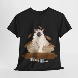 Puede incluir: Camiseta negra con un gato blanco sentado en un bol de masa de pan. El gato tiene ojos azules y está rodeado de pequeños trozos de masa de pan. El texto "Baking Bread" está impreso debajo del gato.